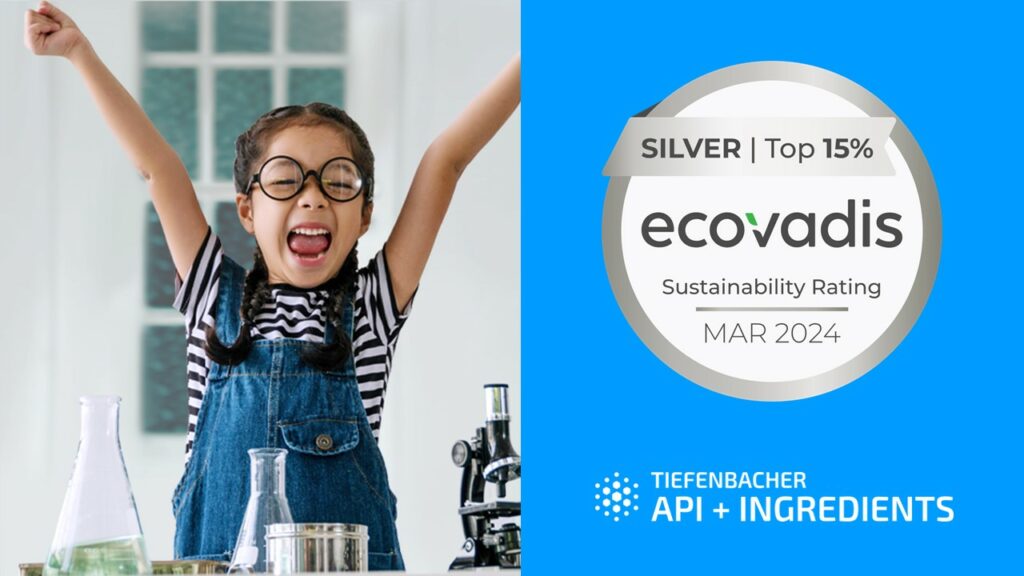 Tiefenbacher Group - A smiling girl with glasses raises her arms in excitement next to science equipment, celebrating patient-centric drug development. Beside her is a silver EcoVadis Sustainability Rating medal for March 2024 and the Tiefenbacher API + Ingredients logo on a blue background.