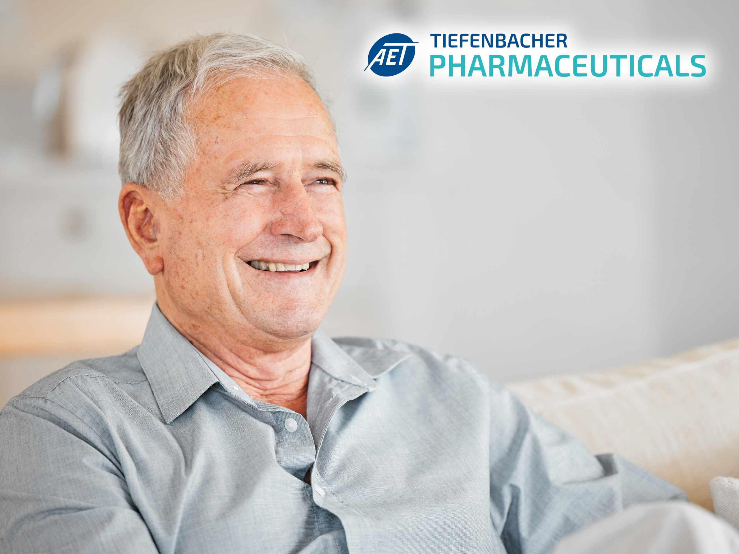 Tiefenbacher Group - An older man with gray hair smiles while sitting on a couch, wearing a light gray shirt. The logo and name "AET Tiefenbacher Pharmaceuticals," a family-owned pharmaceutical company, is visible in the upper right corner.