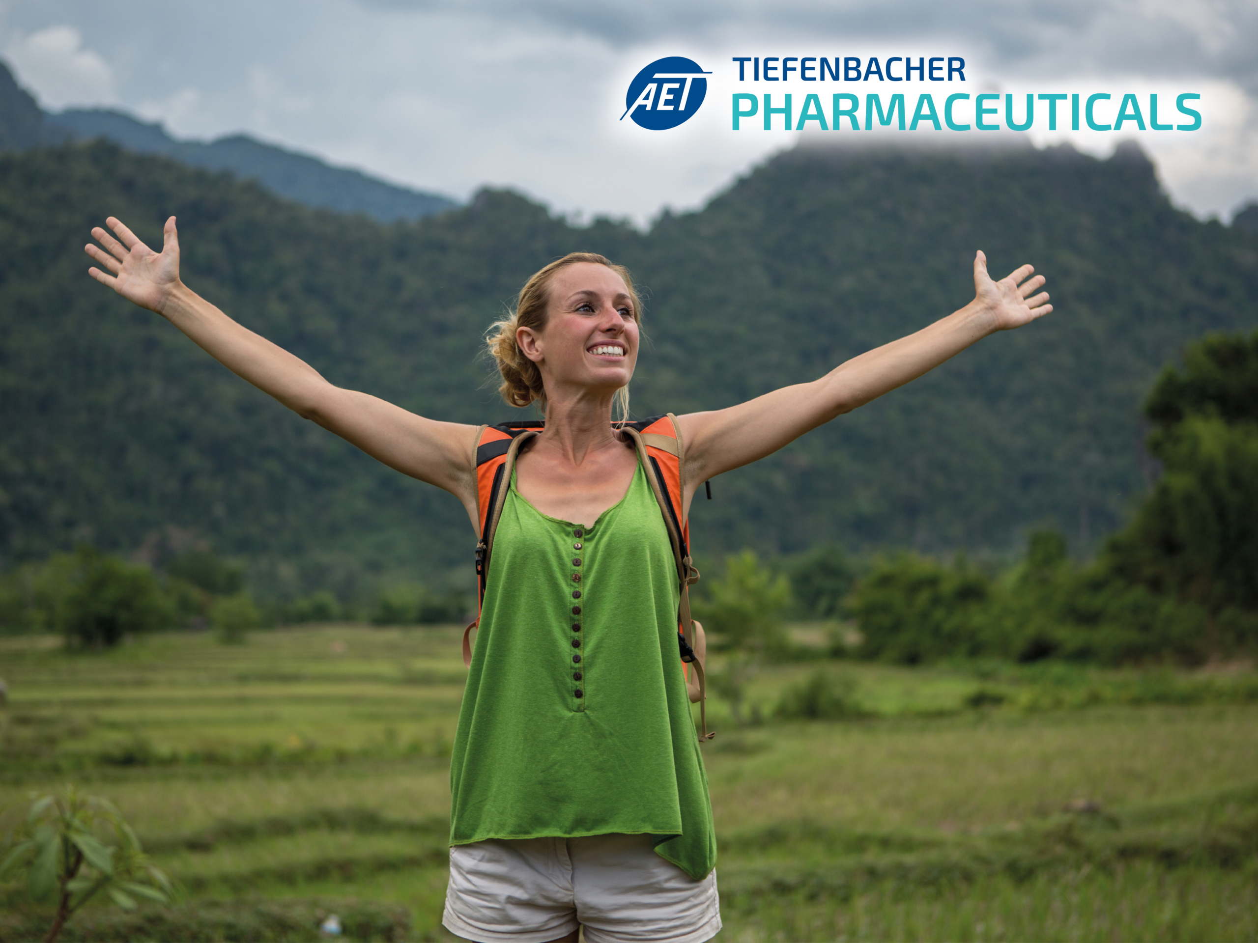 Tiefenbacher Group - A smiling woman in a green top and backpack stands with arms outstretched before lush mountains and fields. The logo and text "Tiefenbacher Pharmaceuticals" highlights their pharmaceutical healthcare solutions in the upper right corner.