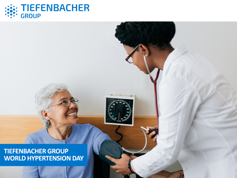 Tiefenbacher Group - A doctor checks an elderly woman's blood pressure with a cuff and stethoscope. Both are smiling, reflecting a patient-centric drug development approach. The text "Tiefenbacher Group World Hypertension Day" appears in the lower left corner.