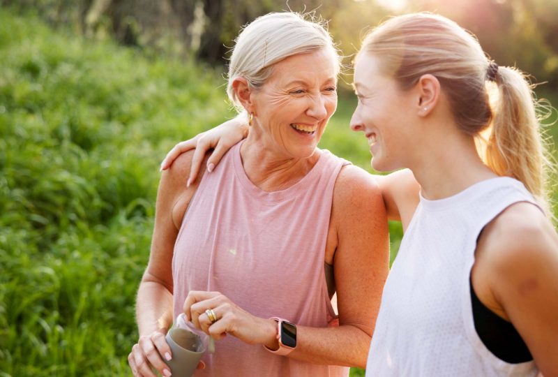 Mature woman, daughter and outdoor on walk for fitness, wellness and exercise in nature with laughing. Female people, conversation and activity together for fresh air, bonding or connection as family