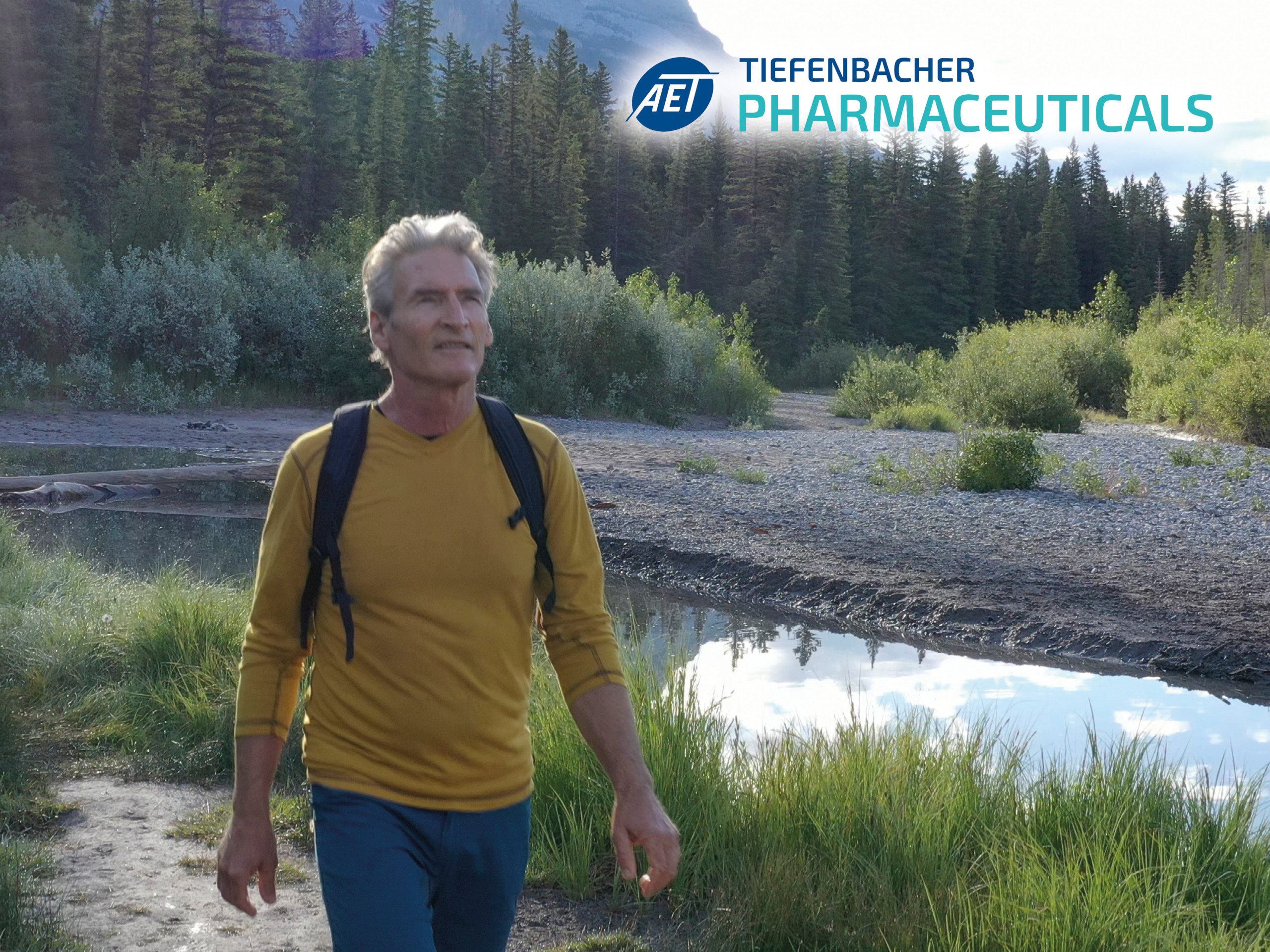 Tiefenbacher Group - An older man with gray hair, wearing a yellow long-sleeve shirt and backpack, walks in a lush riverside landscape. In the corner, the logo and text read "AET TIEFENBACHER PHARMACEUTICALS," a family-owned pharmaceutical company.